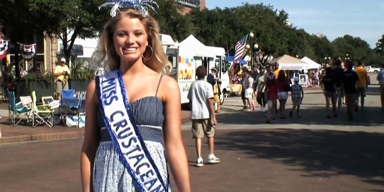 Image from 'The Bay' of a beauty pageant contestant wearing a 'Miss Crustacean' sash and a crab-shaped crown.