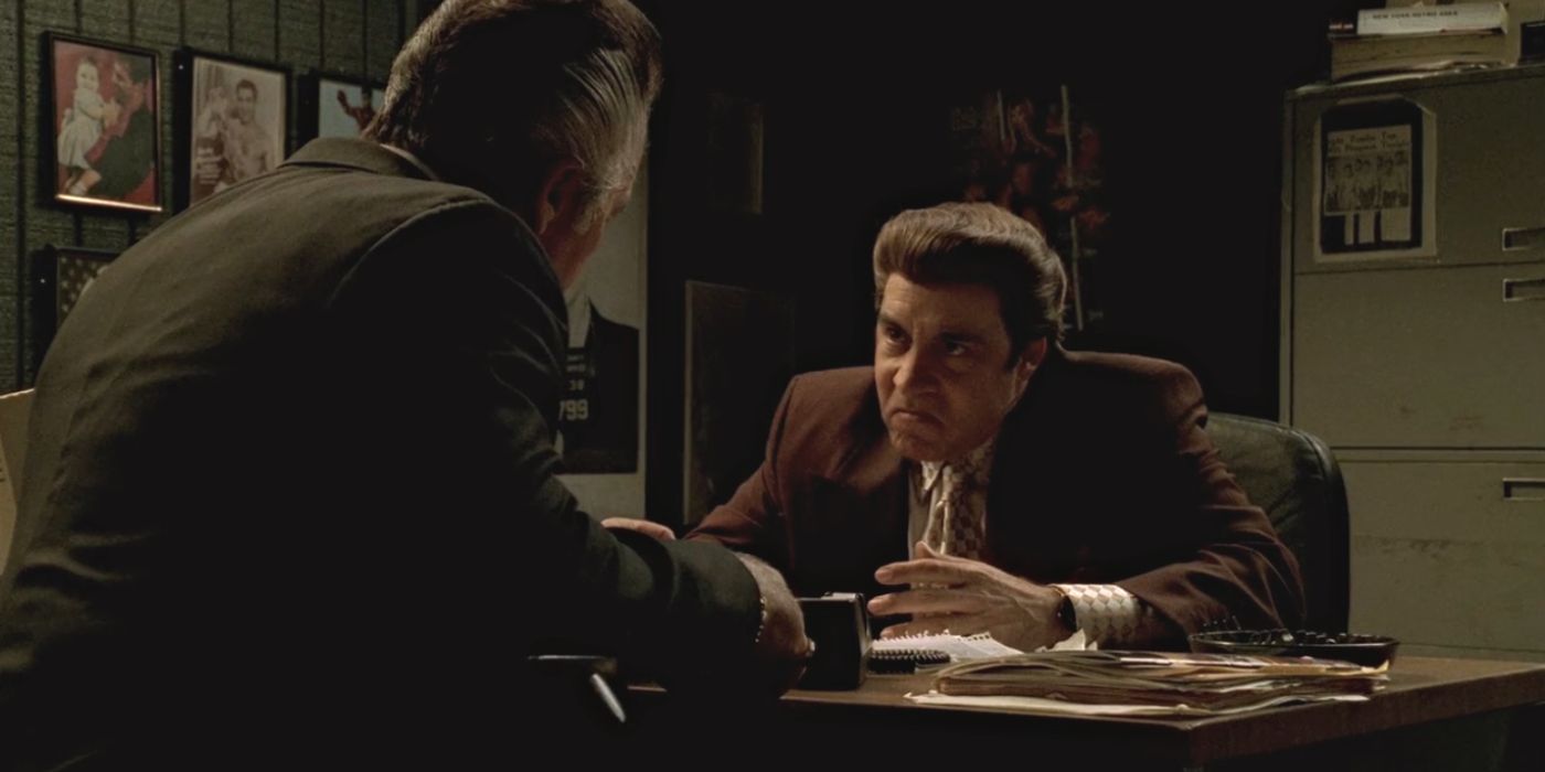 Steven Van Zandt sitting at a desk talking to Tony Sirico in The Sopranos