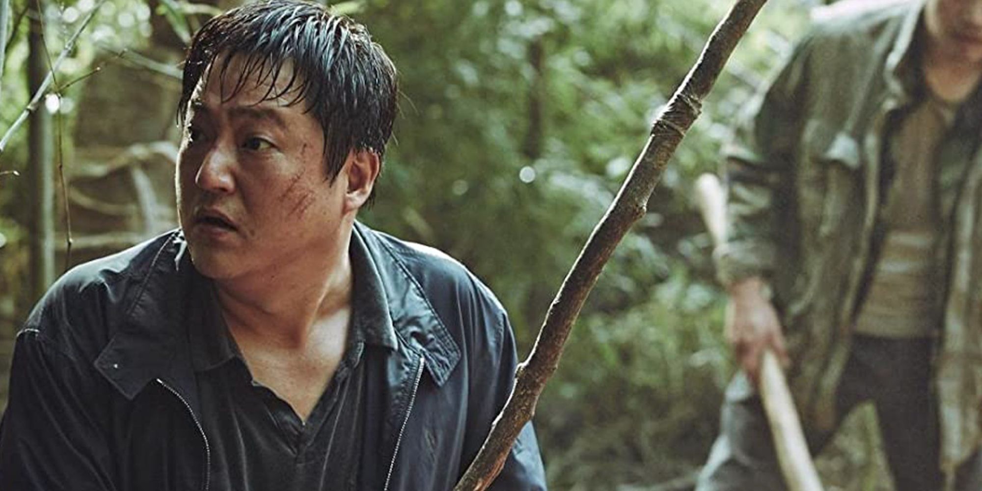 Kwak Do-won holding a long stick in the woods looking scared in The Wailing.