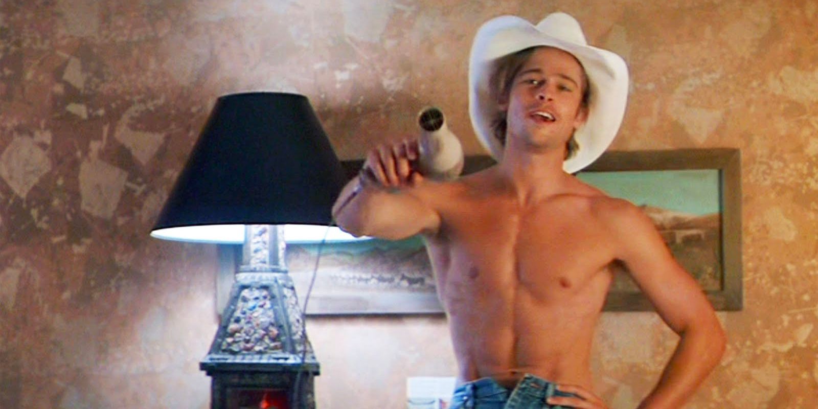 Brad Pitt stands in a hotel wearing a cowboy hat and wielding a hair dryer like a handgun in Thelma & Louise