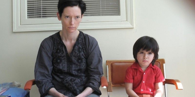 Still from "We Need To Talk About Kevin": Eva (Tilda Swinton) and her young son Kevin (Jasper Newell) sit side by side looking grim.