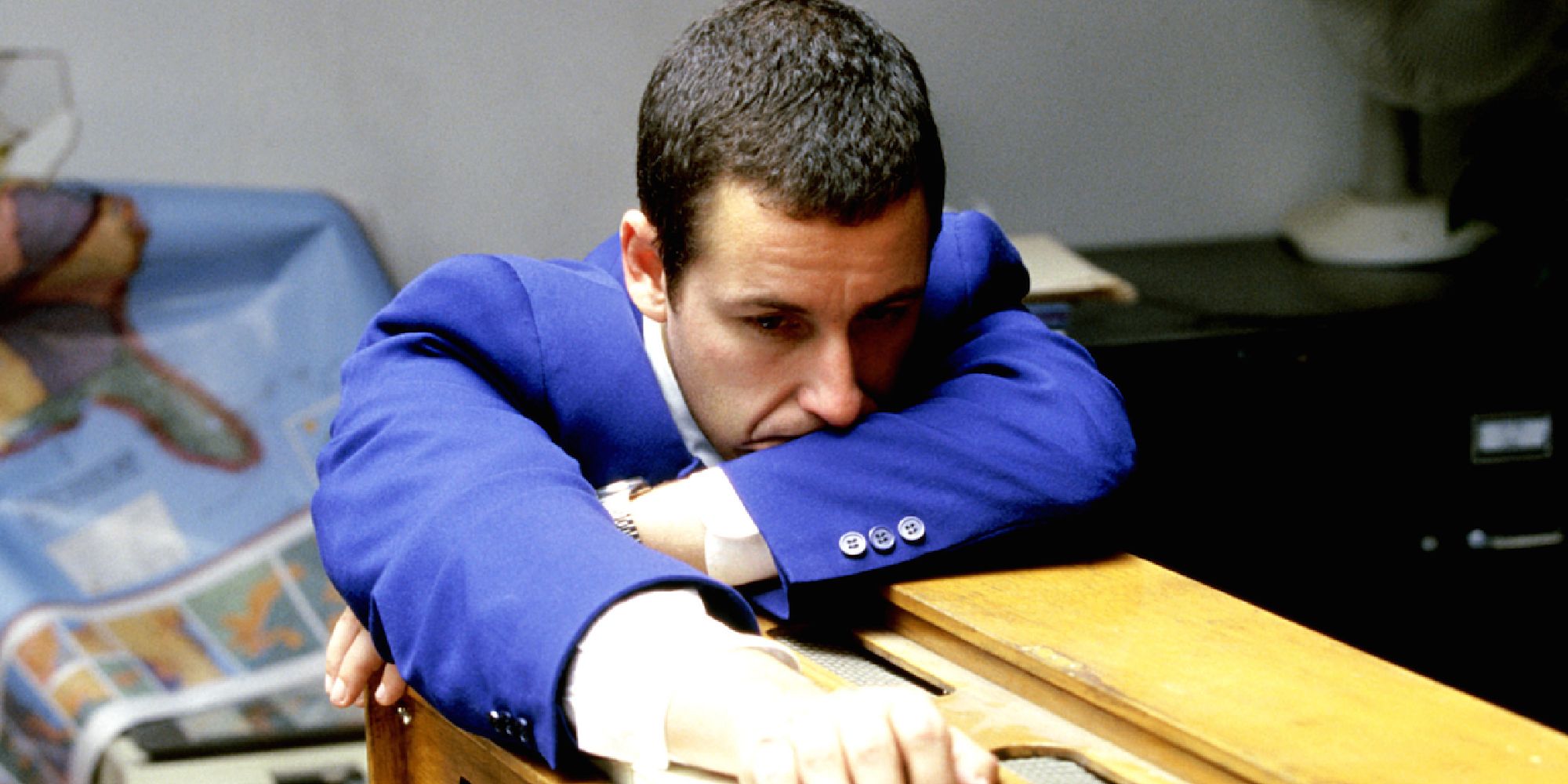 Adam Sandler in 'Punch Drunk Love' slumped over on a desk looking sad.