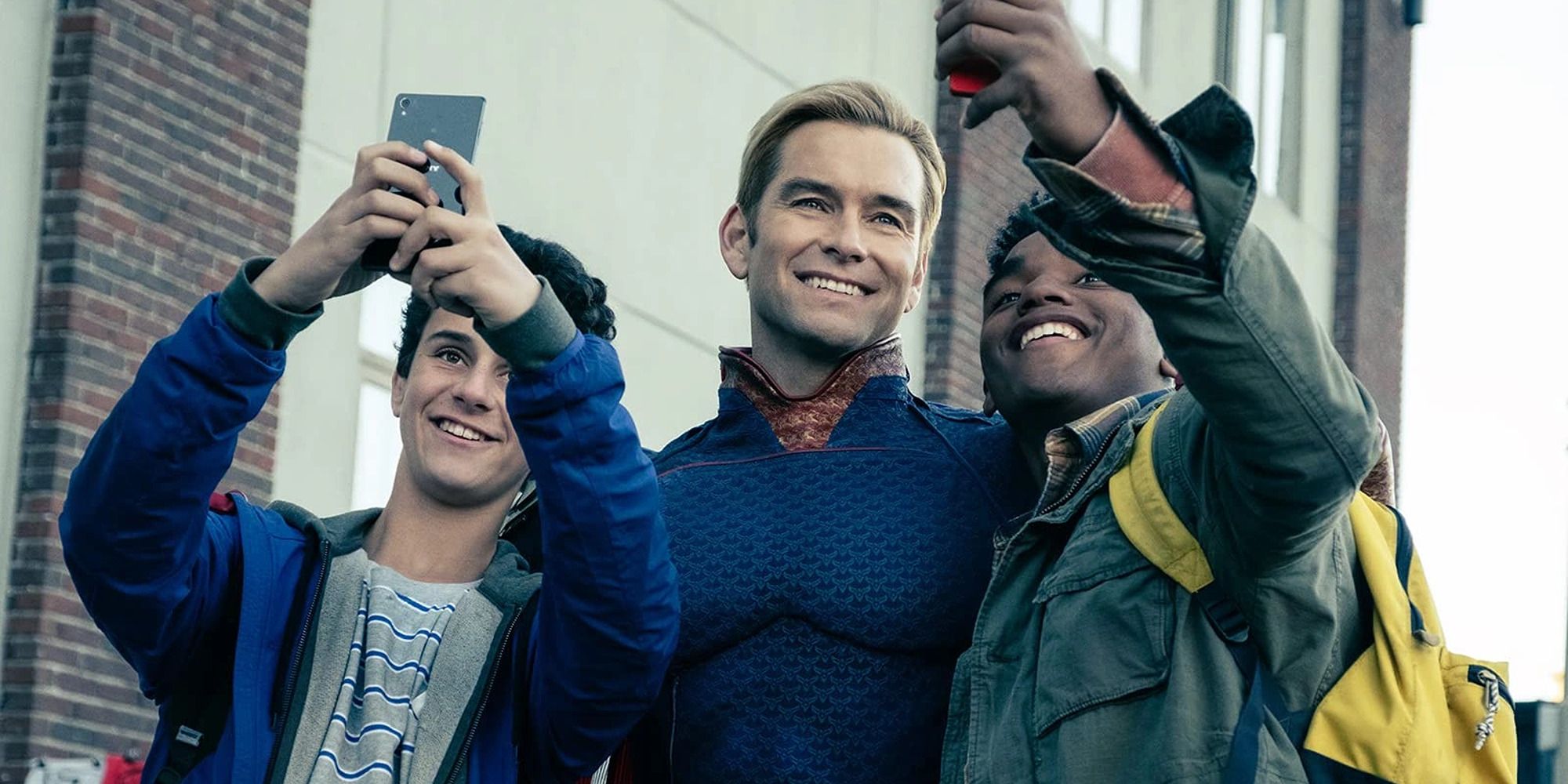 Homelander smiling between two teens taking a selfie with him