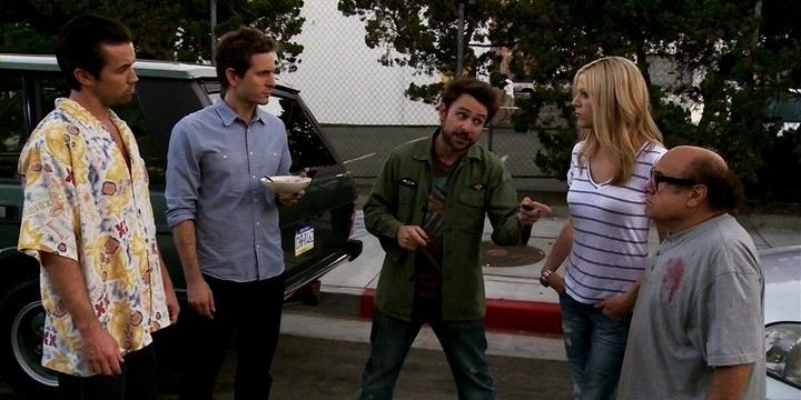 The Gang from 'Always Sunny' stand outside. Dennis holds a bowl of cereal while Charlie points at Frank.