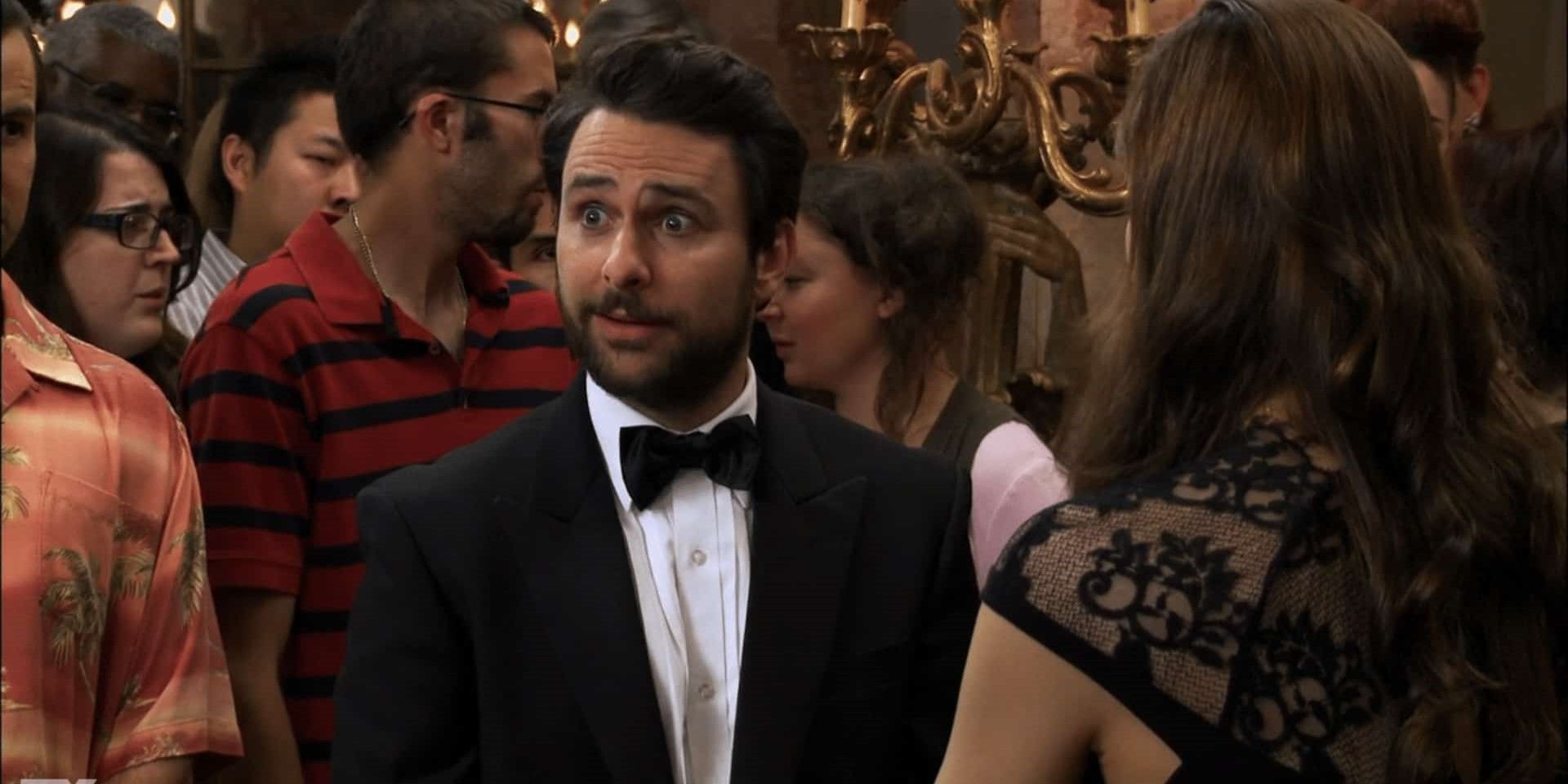 Still from 'It's Always Sunny in Philadelphia': In a room of people, Charlie wears a suit and looks bewildered.
