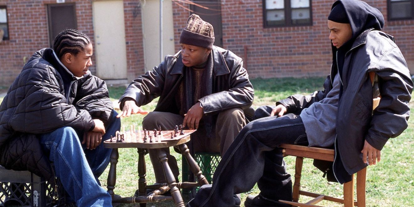 Three drug dealers in Baltimore sit around a chess board in the projects, with one of them teaching the other two how to play.