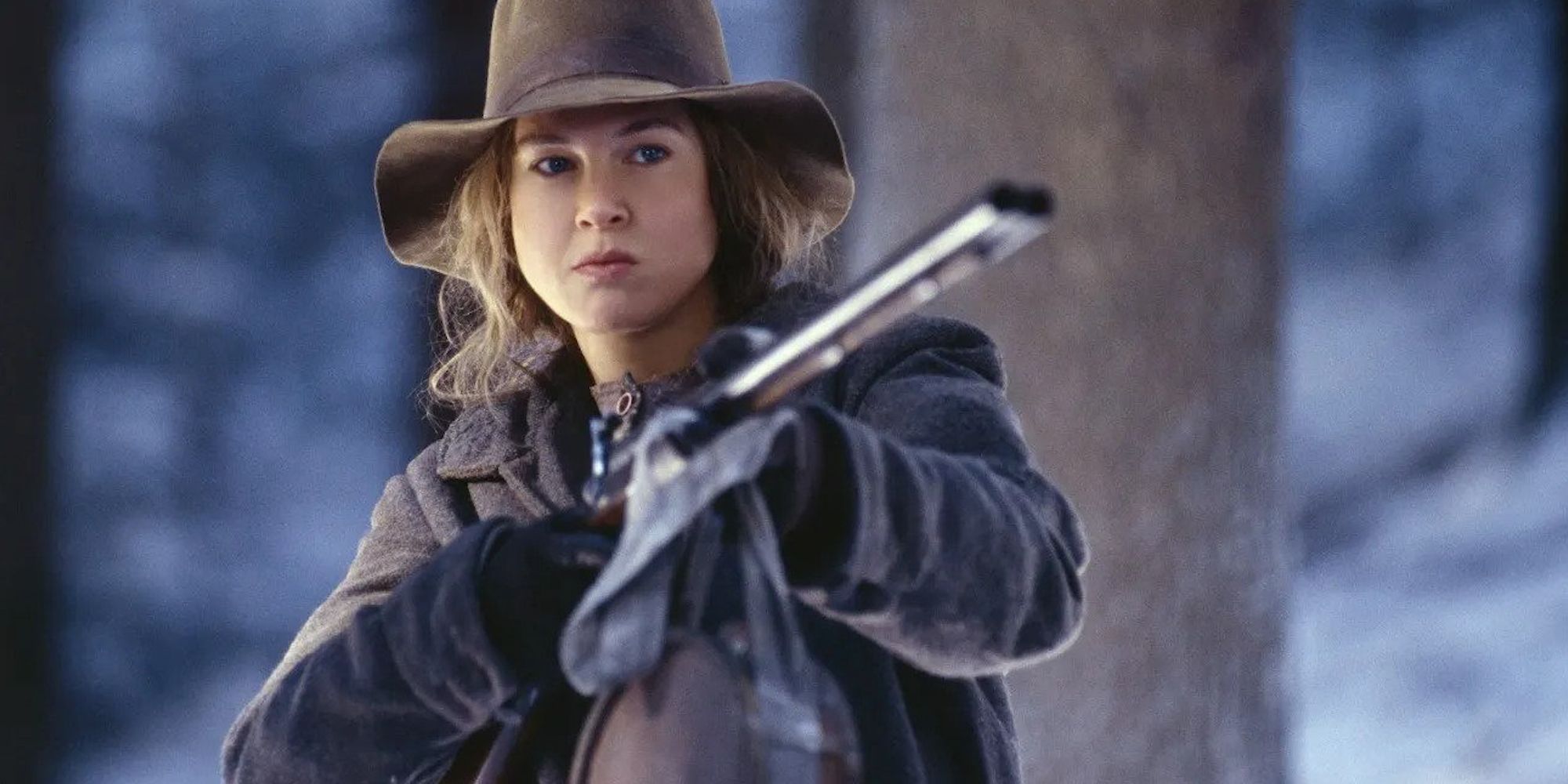 Ruby aiming a rifle at someone off-camera in a forest in Cold Mountain
