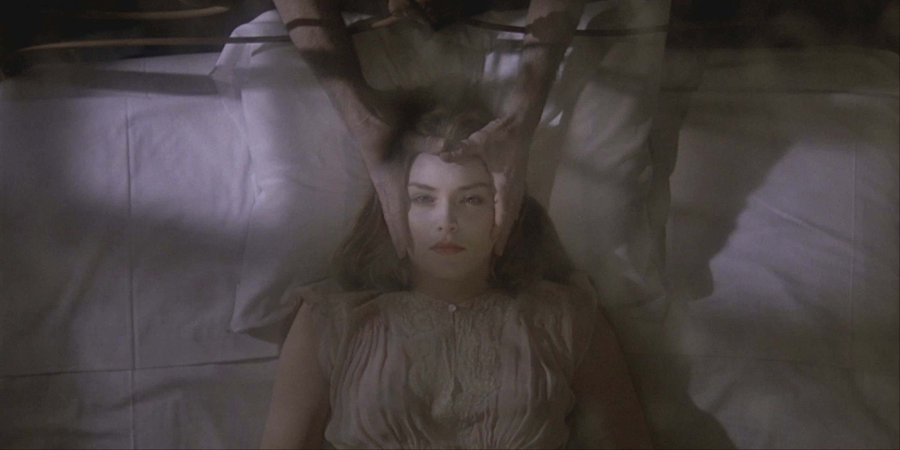 A pair of ghoulish hands holding a woman's face while she lies on a bed in Deadly Blessing.