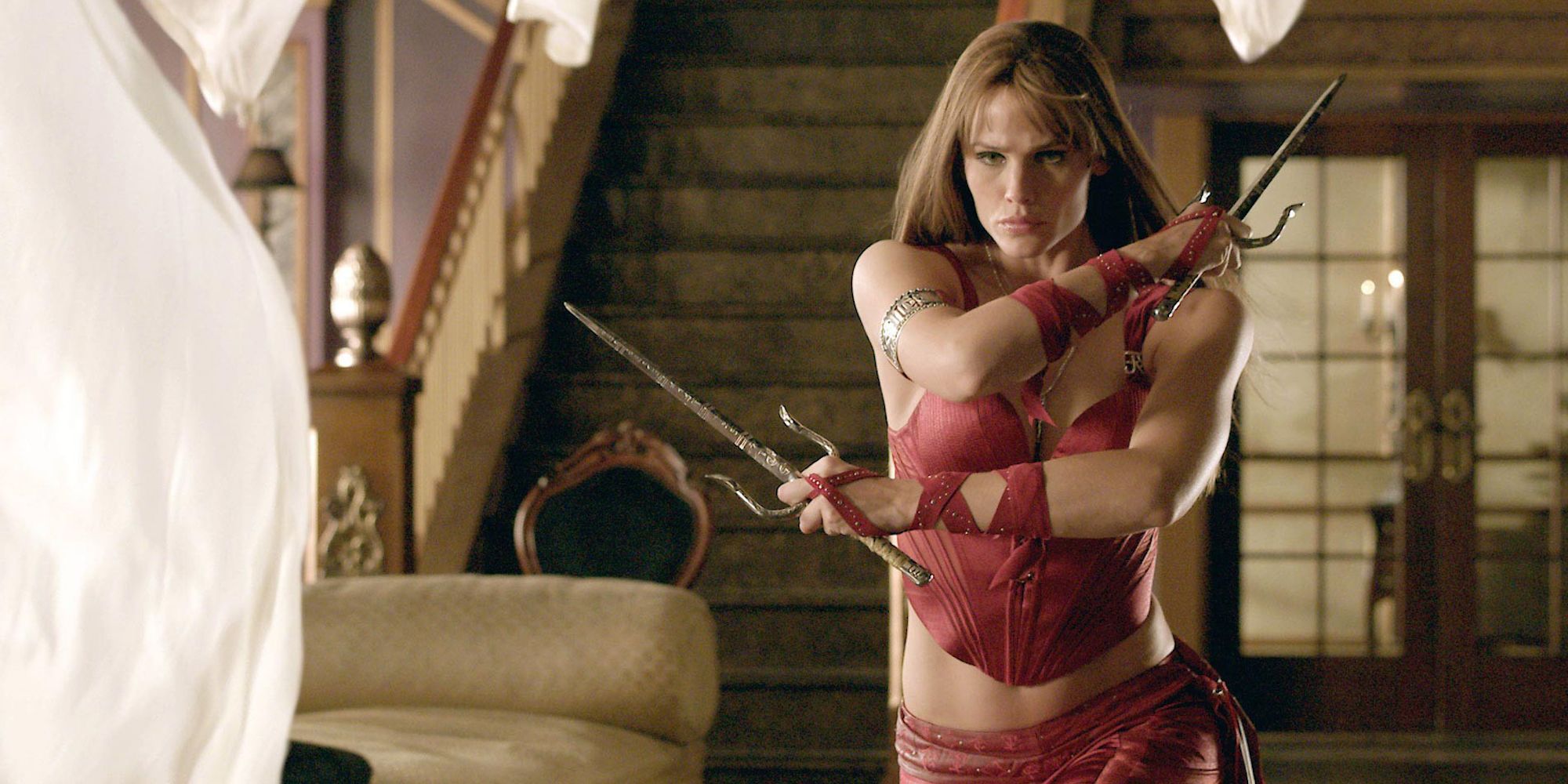 Jennifer Garner as Elektra wielding two sai and walking towards something off-camera in the film 'Elektra.'