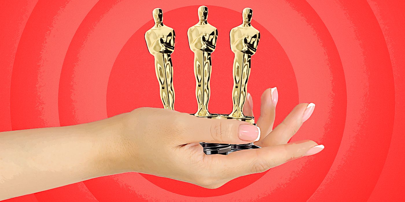 A hand holding three Oscar statuettes on a red background