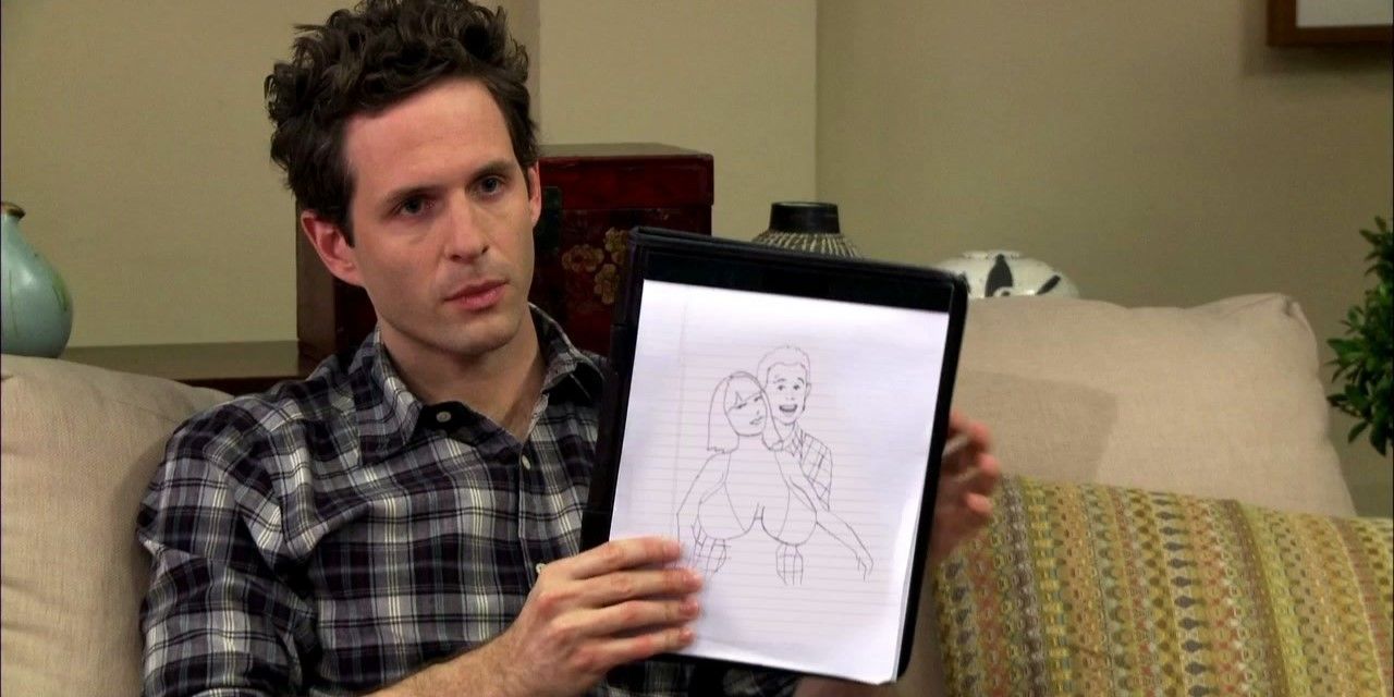 Still from 'It's Always Sunny in Philadelphia': Dennis sits on a couch holding a cartoon of himself and a woman with enormous breasts.