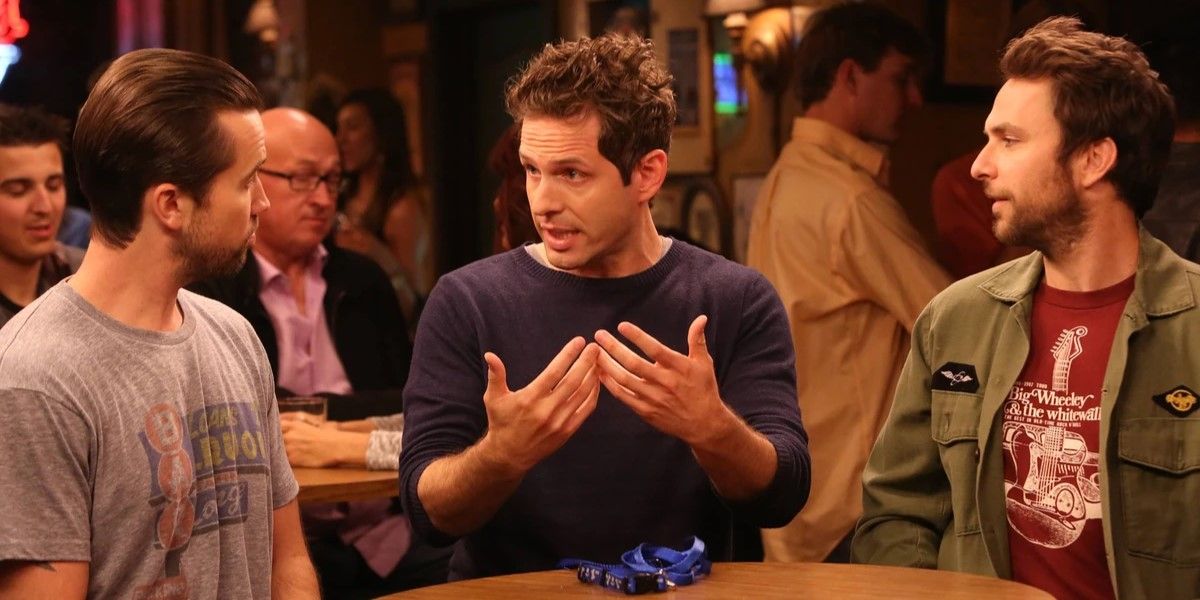 Still from 'It's Always Sunny in Philadelphia': Dennis explains something to Charlie and Mac as they sit at a table.
