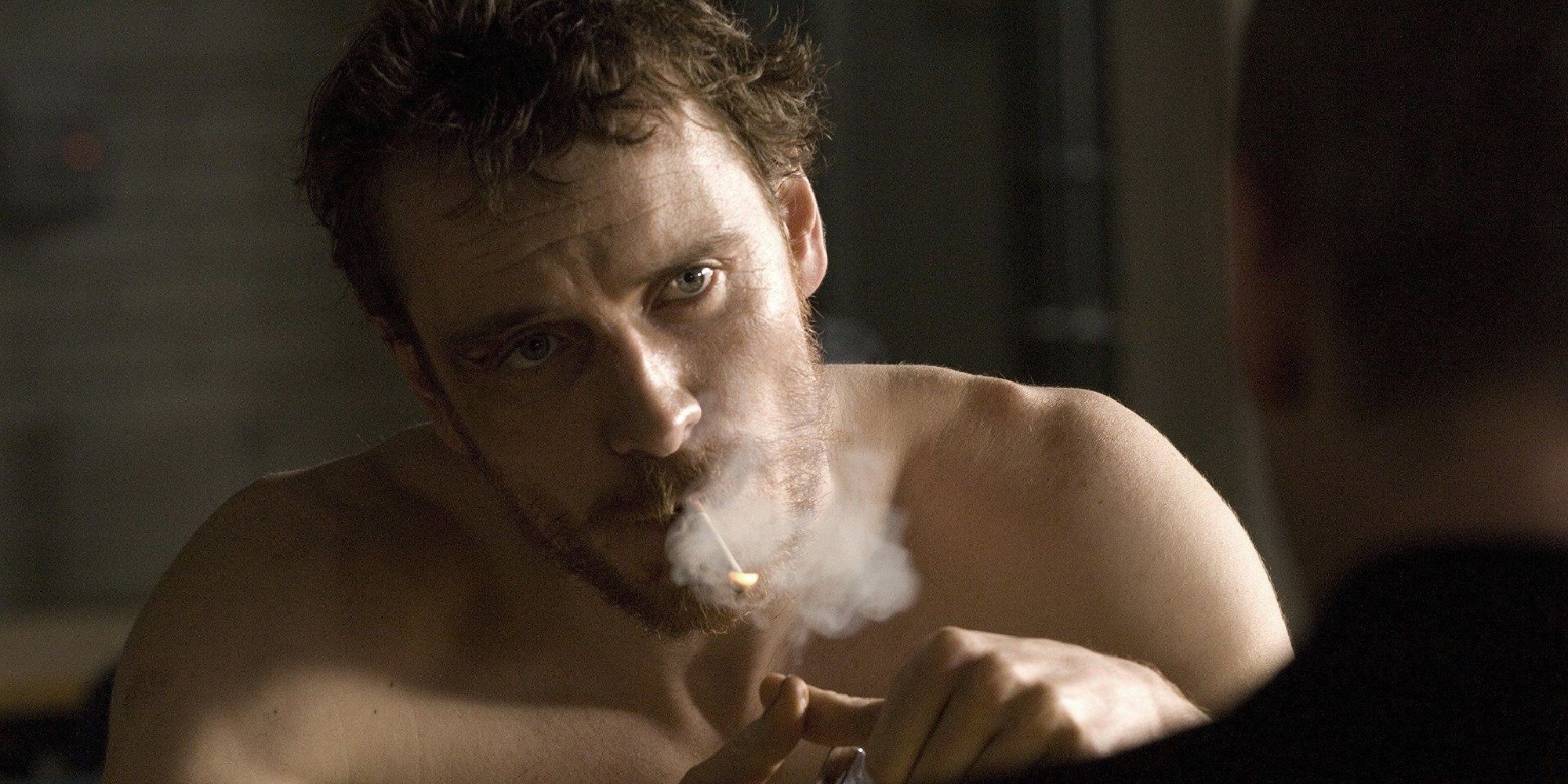 Michael Fassbender as Bobby Sands smoking and looking somberly at someone off camera in the film Hunger - 2008