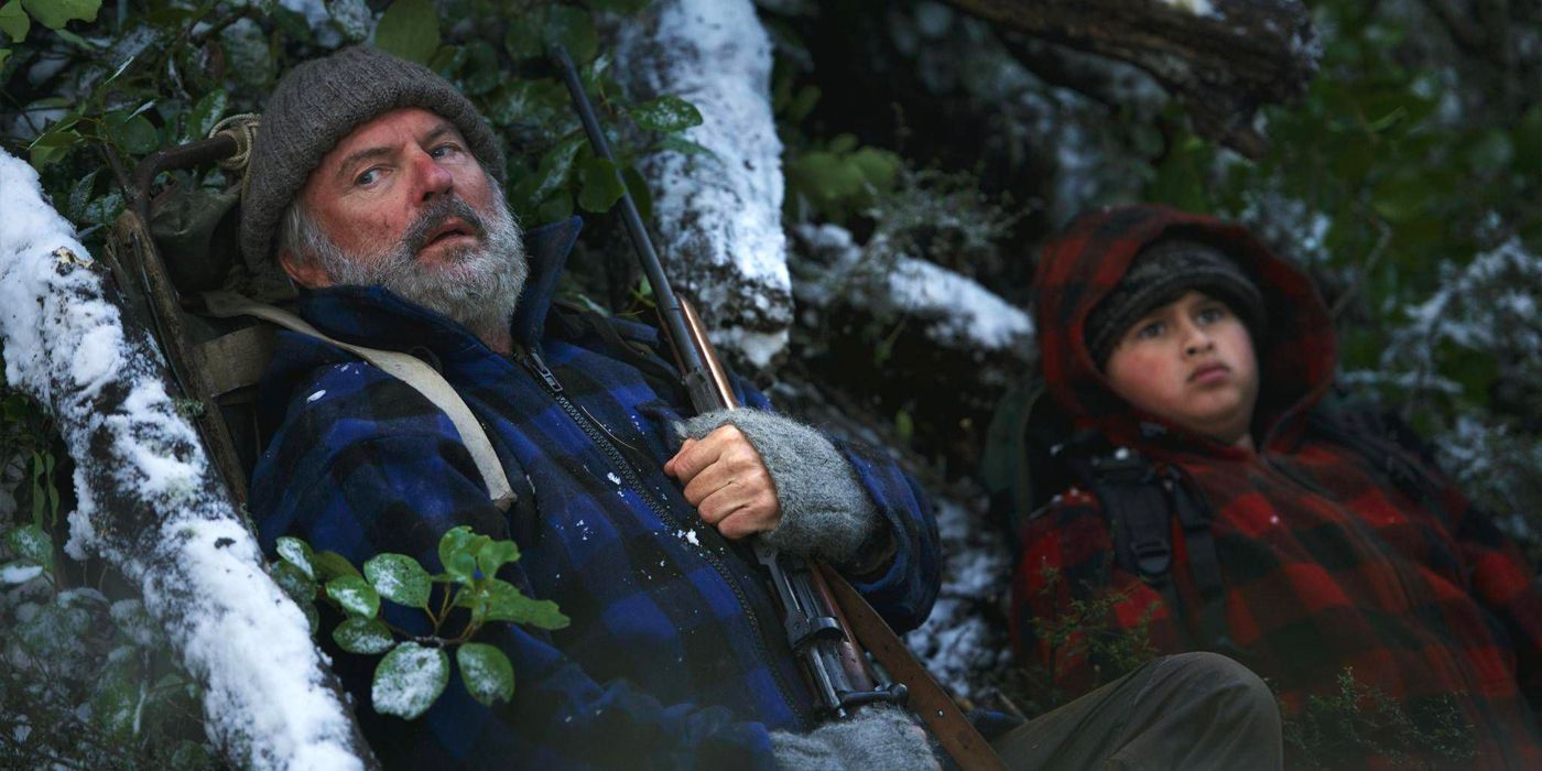 Julian Dennison and Sam Neill lean against a rock hiding in Hunt for the Wilderpeople