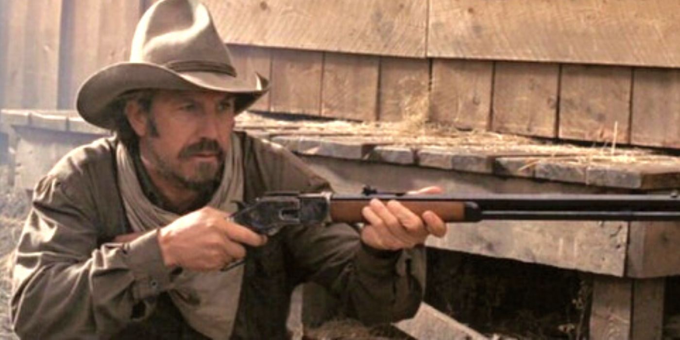 Kevin Costner crouching down holding a rifle in Open Range