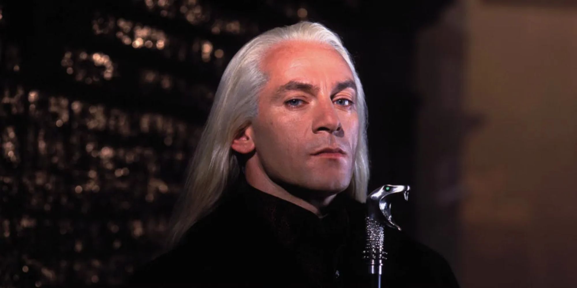 Lucius Malfoy lurks in the shadows, holding his famous snake-headed wand case