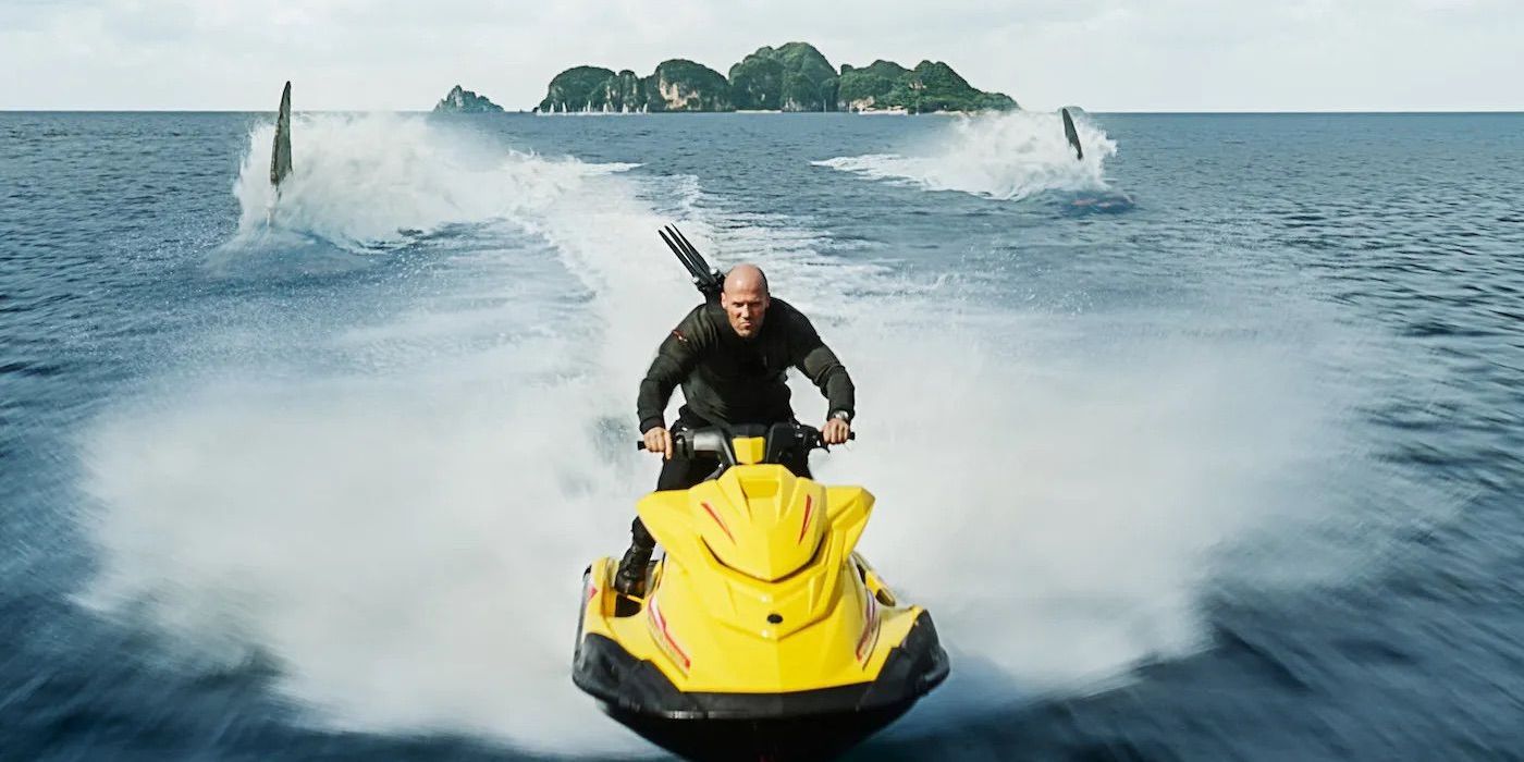 Jason Statham on a waverider trying to outrun two shark fins in The Meg 2 The Trench