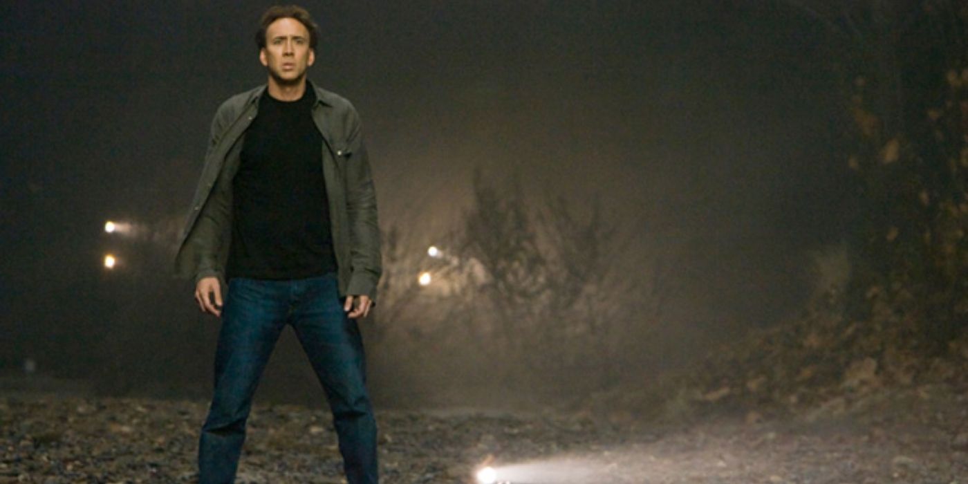 Nicolas Cage standing in a forest with a flashlight on the ground behind him in 'Knowing.' 