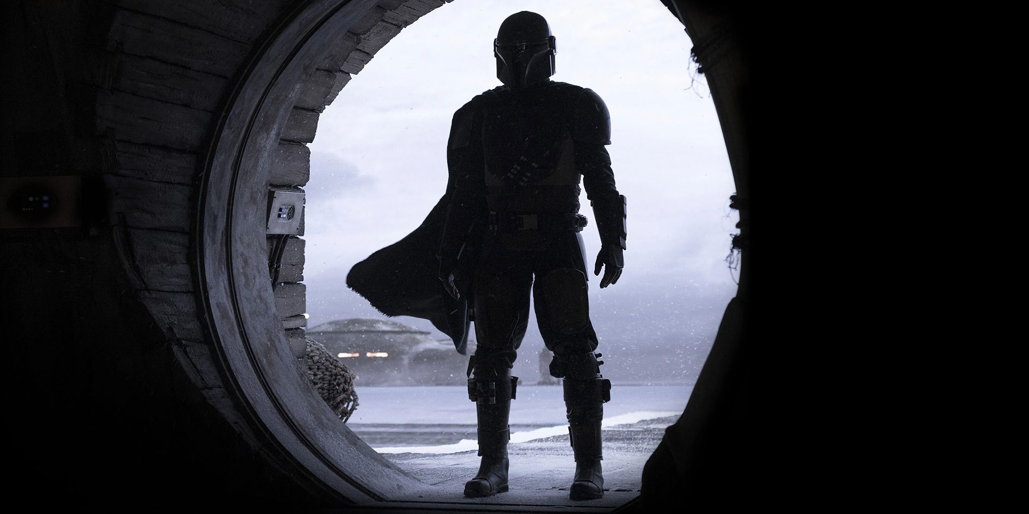 Pedro Pascal in armor in The Mandalorian standing in the middle of a circular door hole.