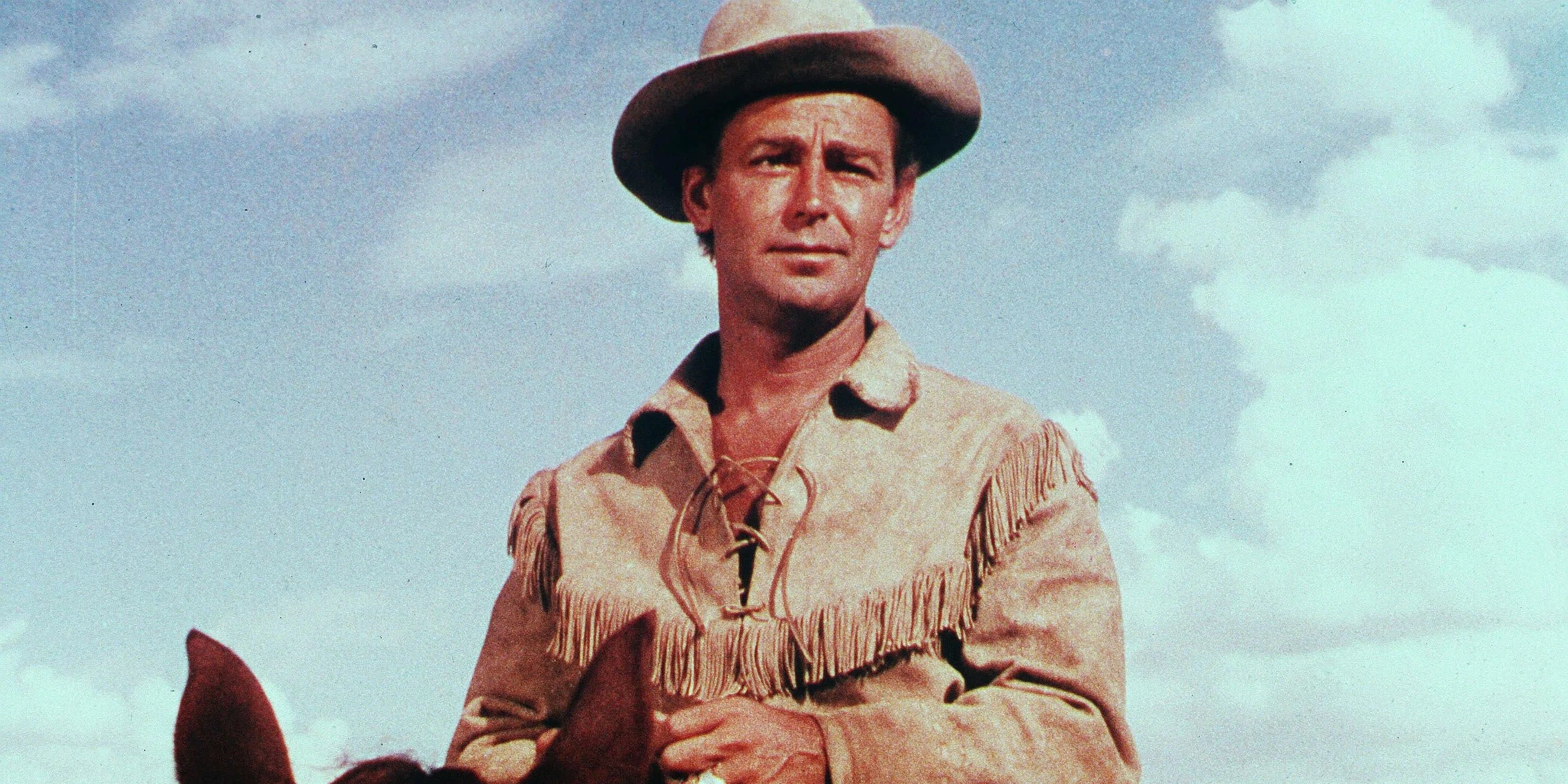 Shane (Alan Ladd) wears a light hat and jacket as he rides on horseback on a sunny day.
