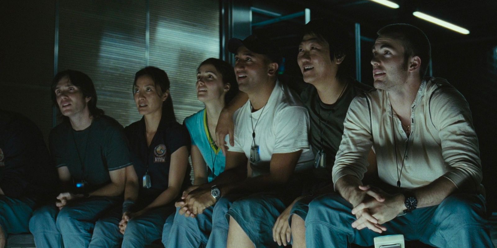 Une équipe de scientifiques assis dans une salle de jeux sur leur vaisseau spatial, souriant en regardant quelque chose ensemble.