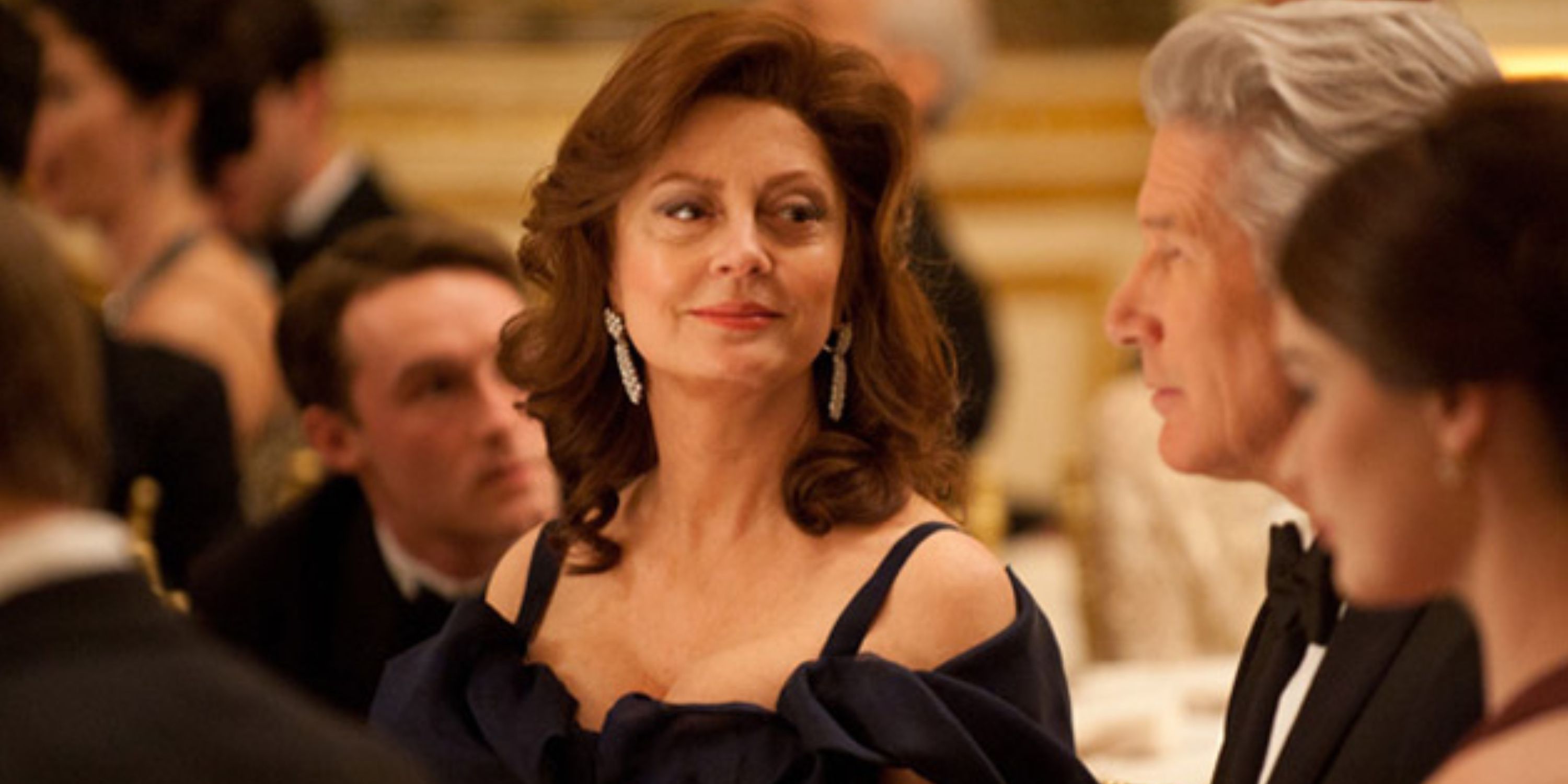 Susan Sarandon as Ellen Miller in Arbitrage, she is at a fancy dinner wearing a flattering dress, sitting with others at a table