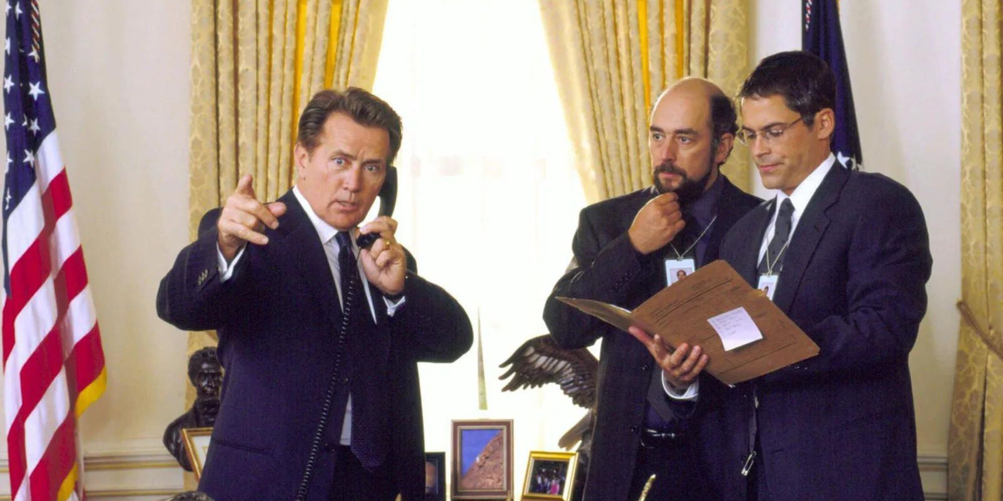 President Bartlet is on the phone while Sam Seaborn and Toby Ziegler stand beside him in the oval office