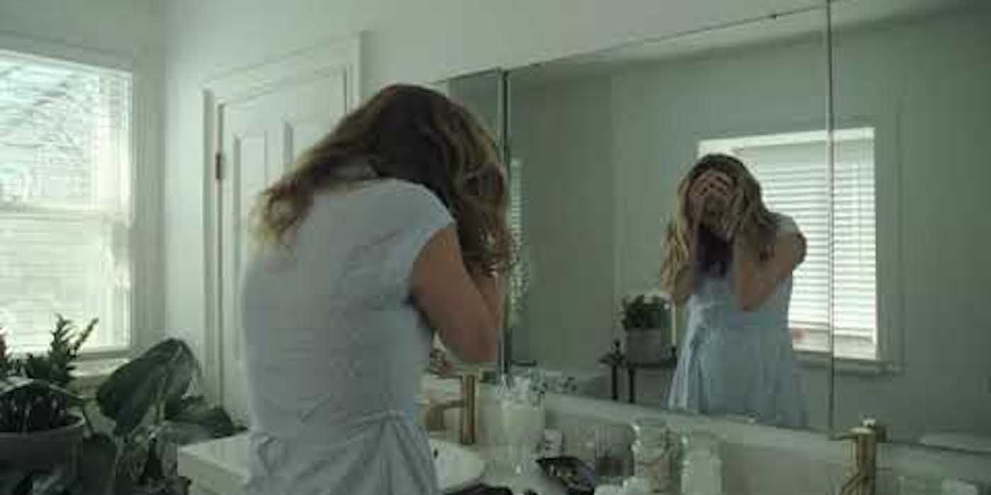 A woman holding her head in desperation in front of the mirror in The Lodge