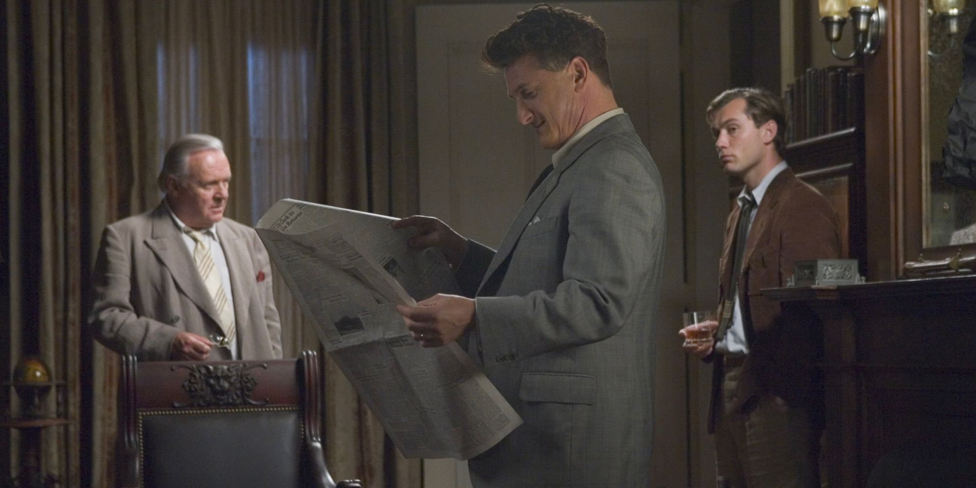 Un homme politique américain des années 1940 lit le journal tandis que deux de ses conseillers se tiennent derrière lui.