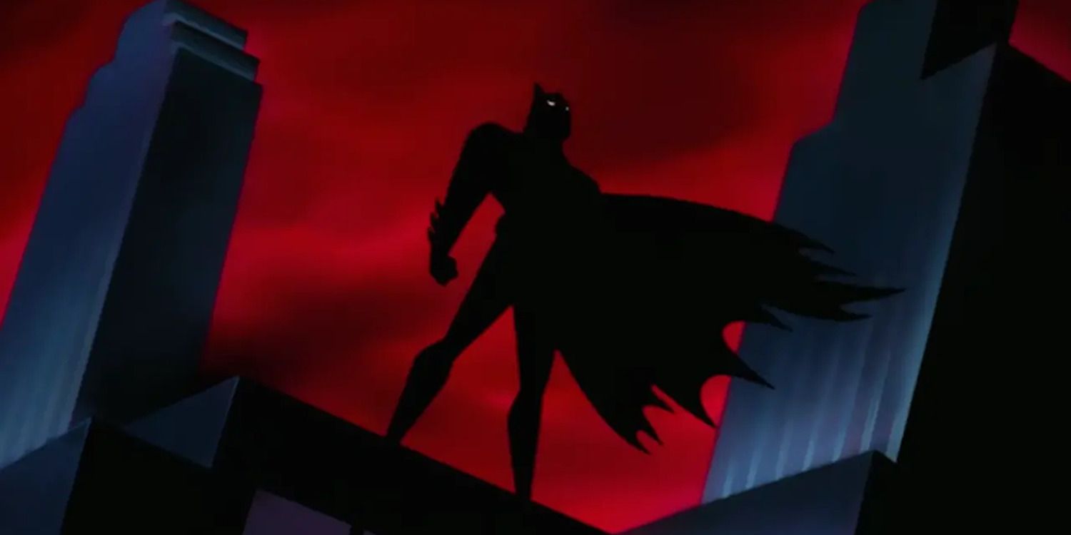 Batman's shadow standing atop a rooftop in front of buildings