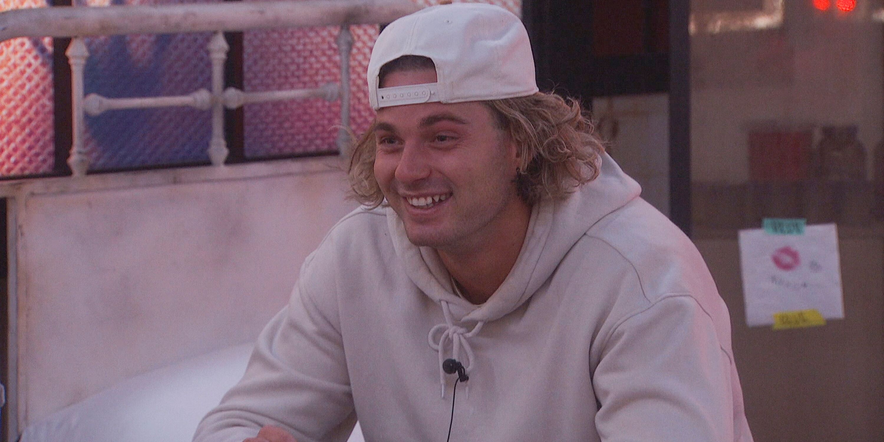 Matt Klotz sourit dans un sweat à capuche blanc, assis sur un lit « Big Brother 25 »