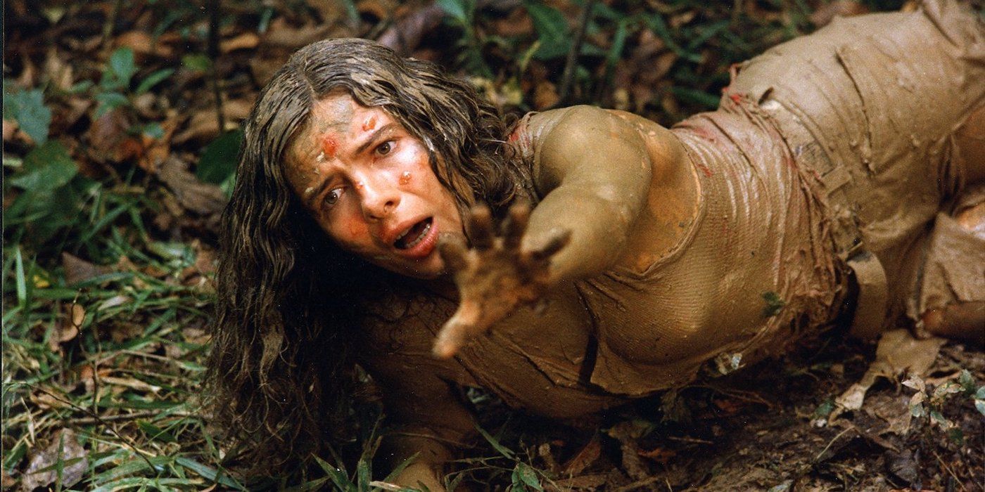 Lorraine De Selle as Gloria Davis, lying on the ground, covered in mud and reaching out in anguish in Cannibal Ferox