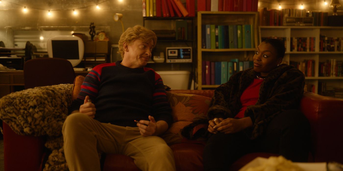 Rhys Darby and Gabrielle Graham sit on a couch in in 'Relax I'm From the Future'