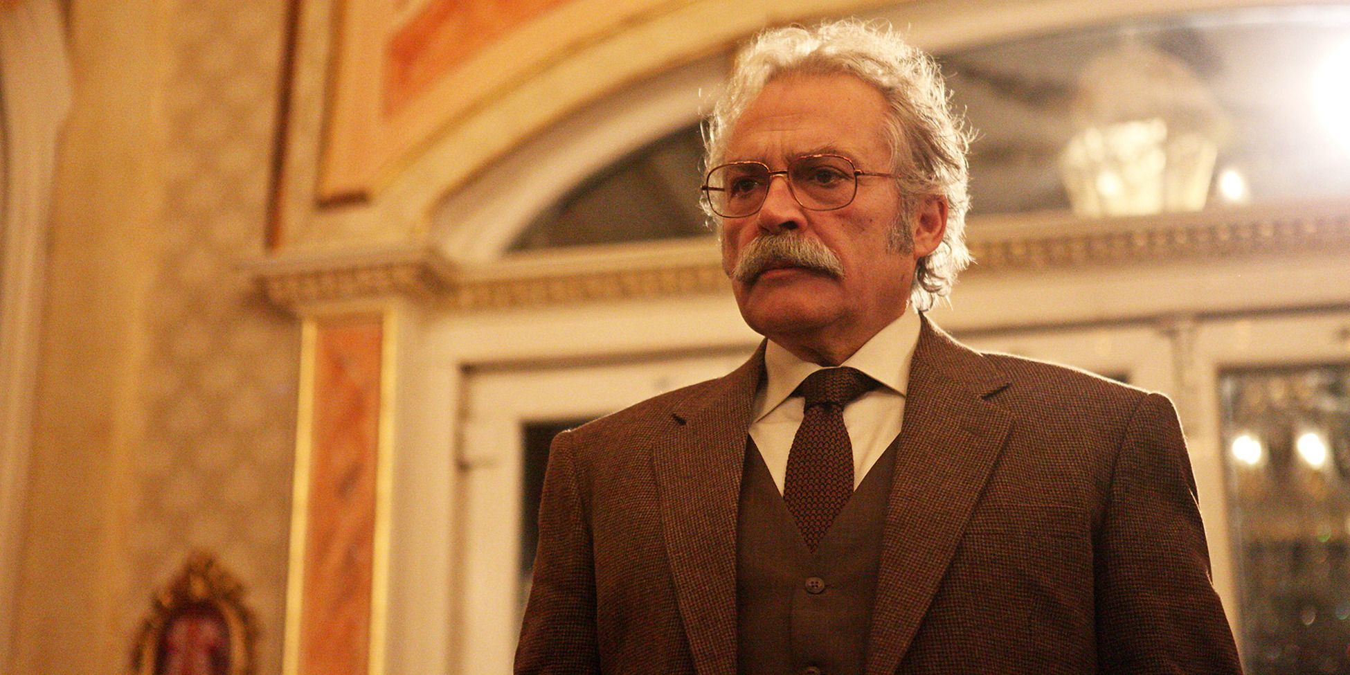 Haluk Bilginer in &lsquo;Sahsiyet&rsquo; standing in front of a door wearing a brown suit