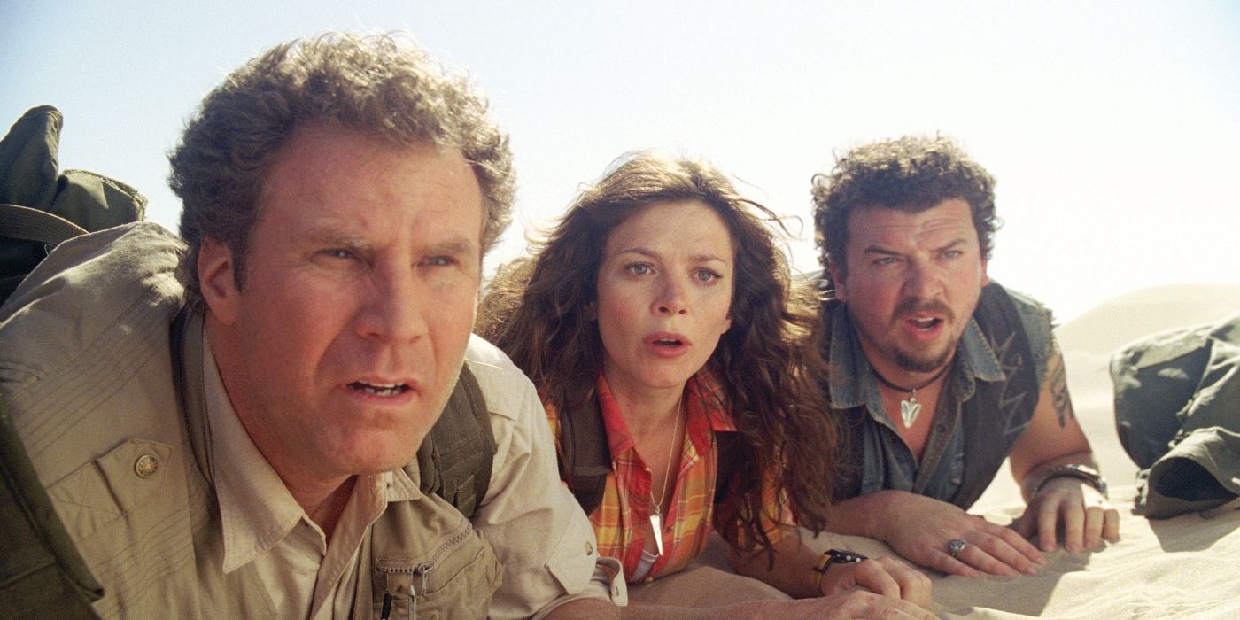 The cast lay on their stomachs on the ground and look at something in the distance in Land of the Lost. 