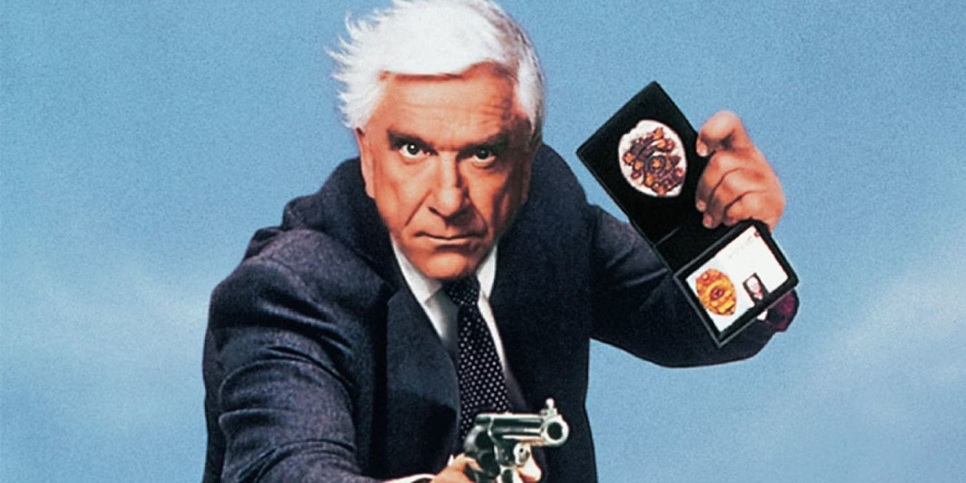 Leslie Nielsen as a police detective with a suit, a gun, and showing his badge in The Naked Gun