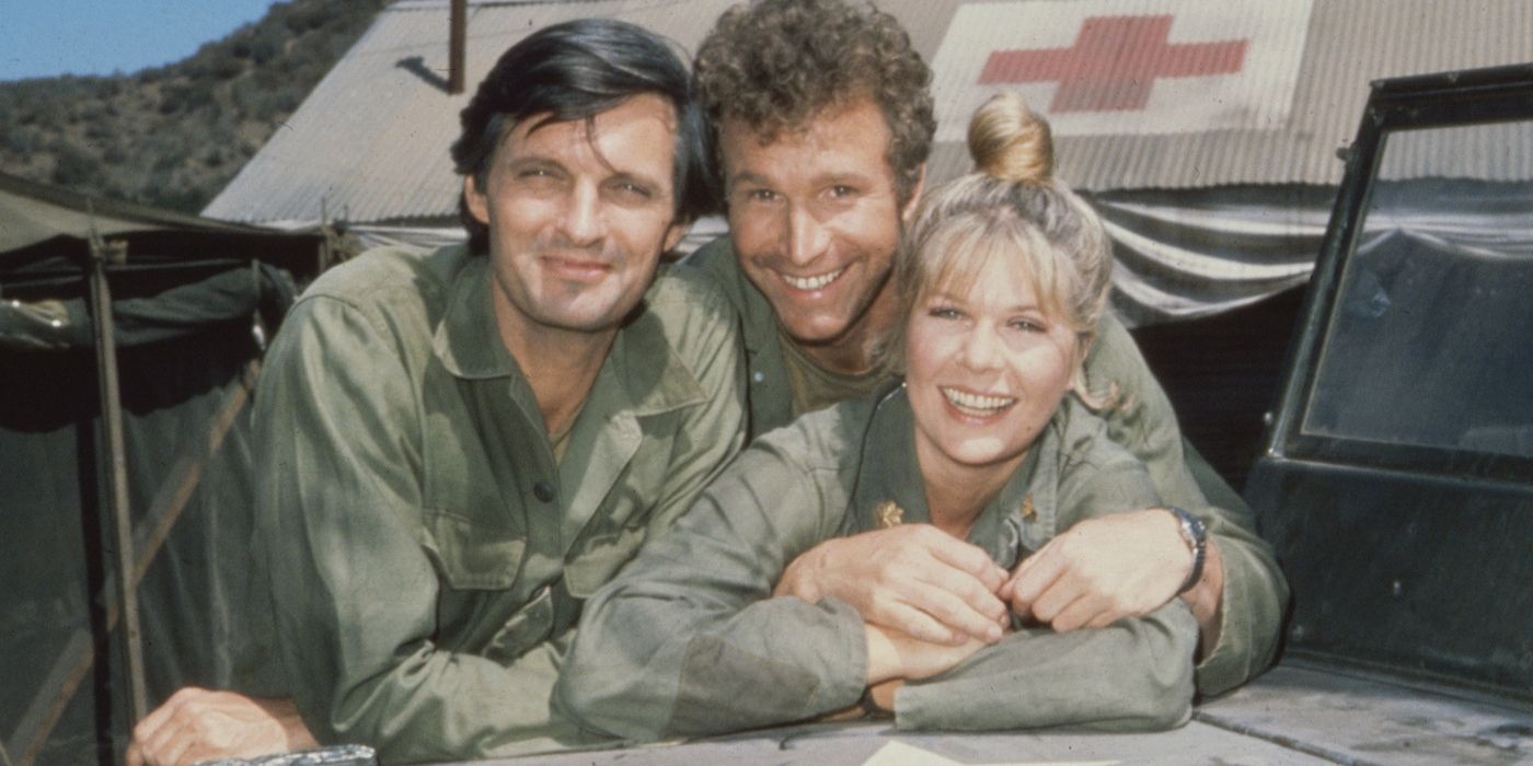 Actors Alan Alda, Loretta Swit, and Wayne Rogers leaning on the hood of a military vehicle on the set of M*A*S*H*