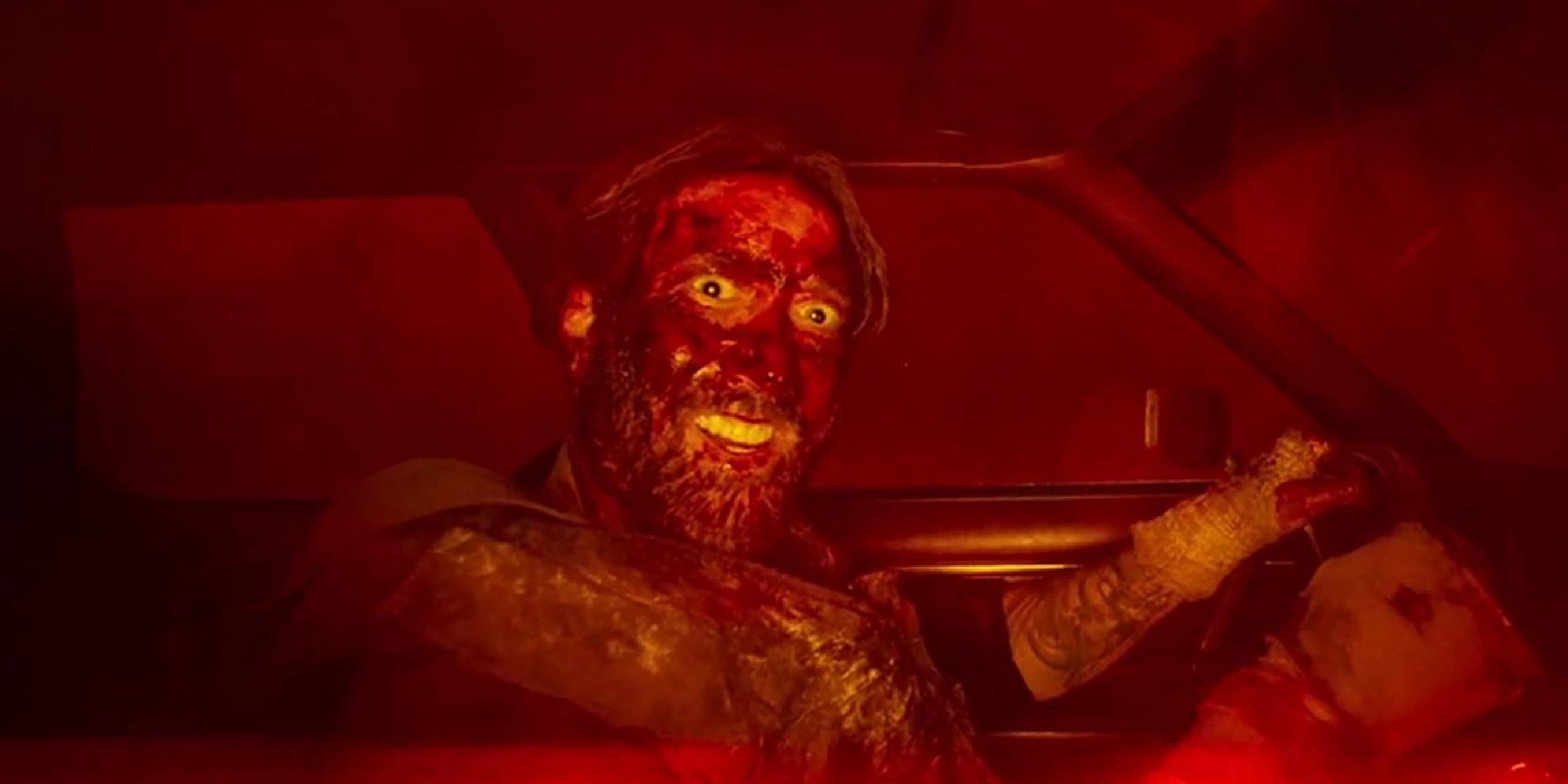 Nicolas Cage as Red sitting behind the wheel of a car smiling and covered in blood in 'Mandy'