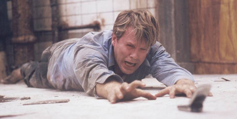 Cary Elwes as Dr. Lawrence Gordon crying and crawling on the floor towards a flip phone in Saw.