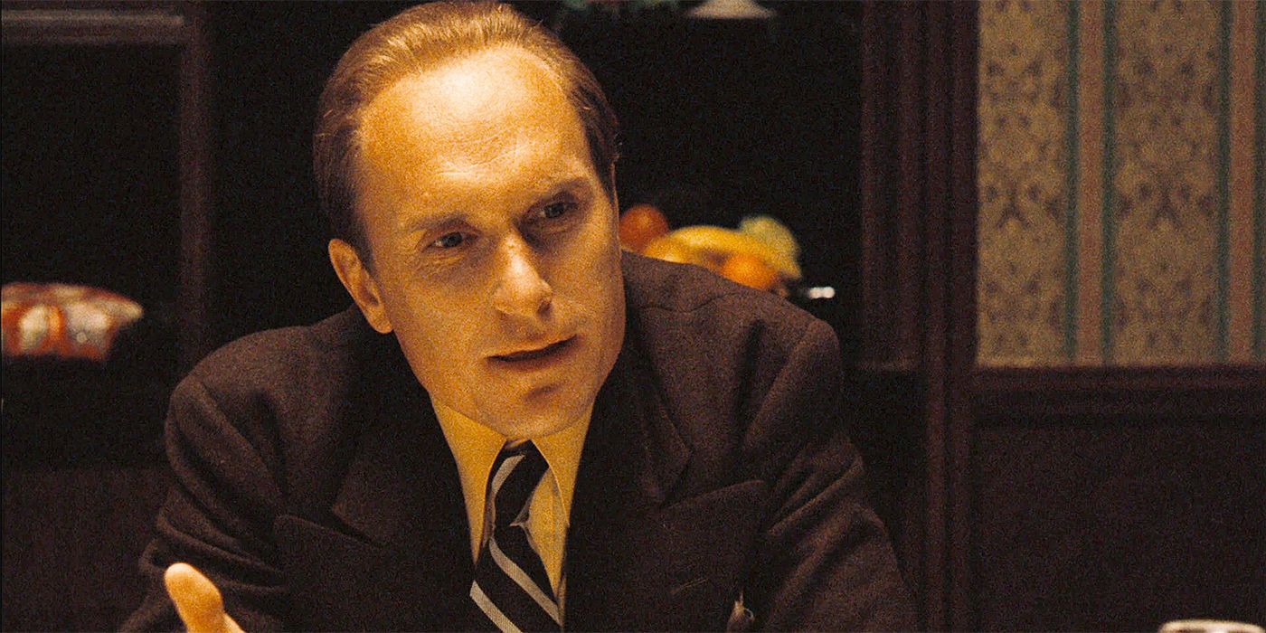 Robert Duvall as Tom Hagen, wearing a suit and sitting at a table in The Godfather