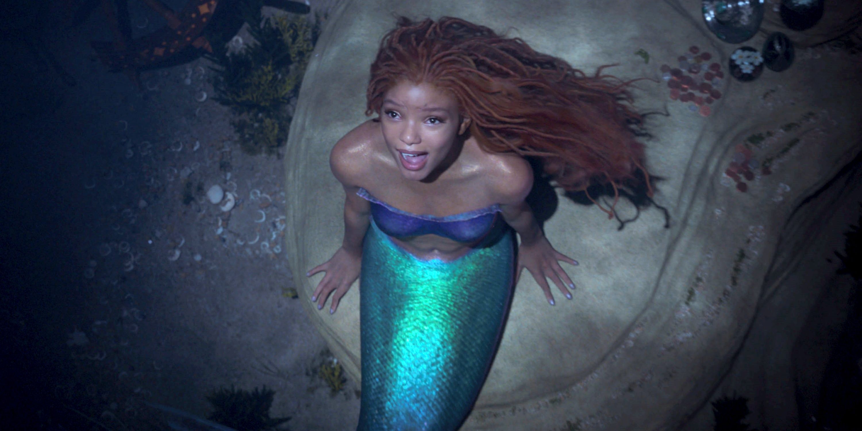 Halle Bailey as Ariel sitting on a rock and singing underneath the sea in The Little Mermaid