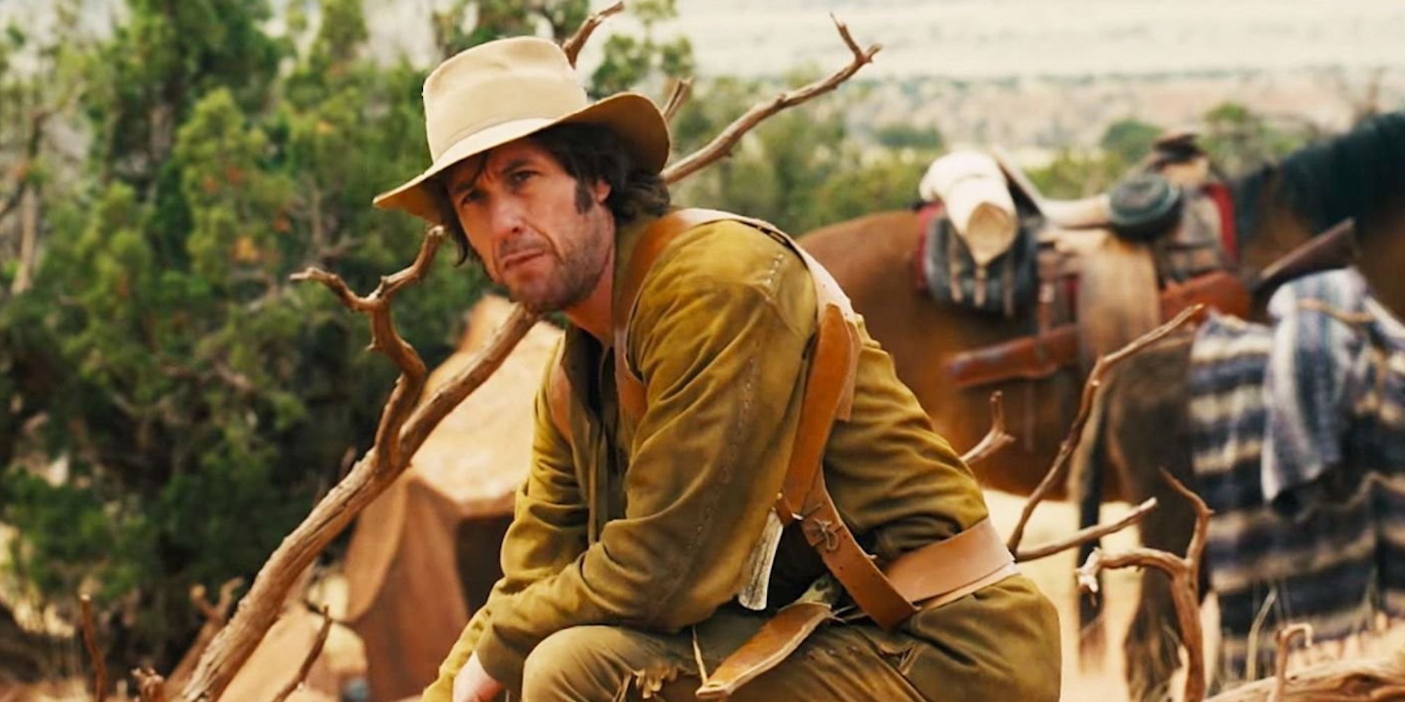 Tommy, sitting by a horse and looking serious in The Ridiculous 6