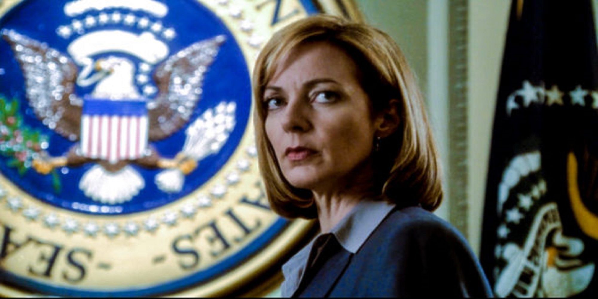 Allison Janney as Press Secretary C.J. Cregg, standing to the side with the presidential seal looming over her, in The West Wing