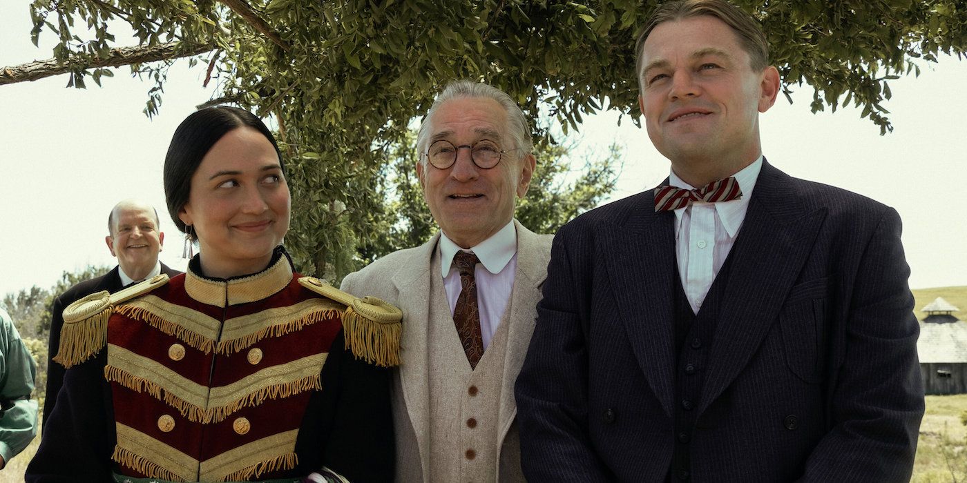 Lily Gladstone, Robert De Niro & Leonardo DiCaprio standing together outdoors in Killers of the Flower Moon