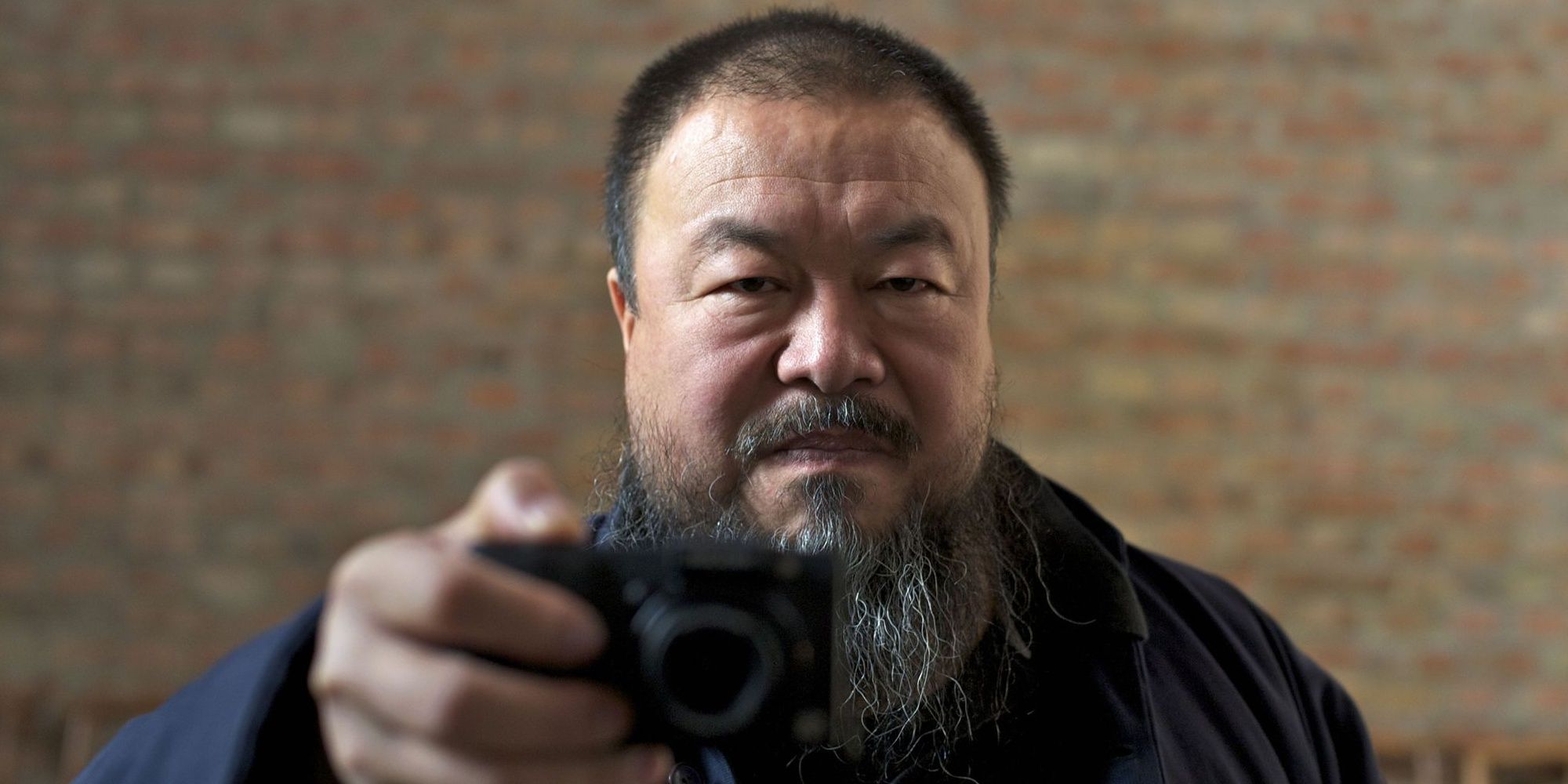 Ai Weiwei showing a small camera and smiling.