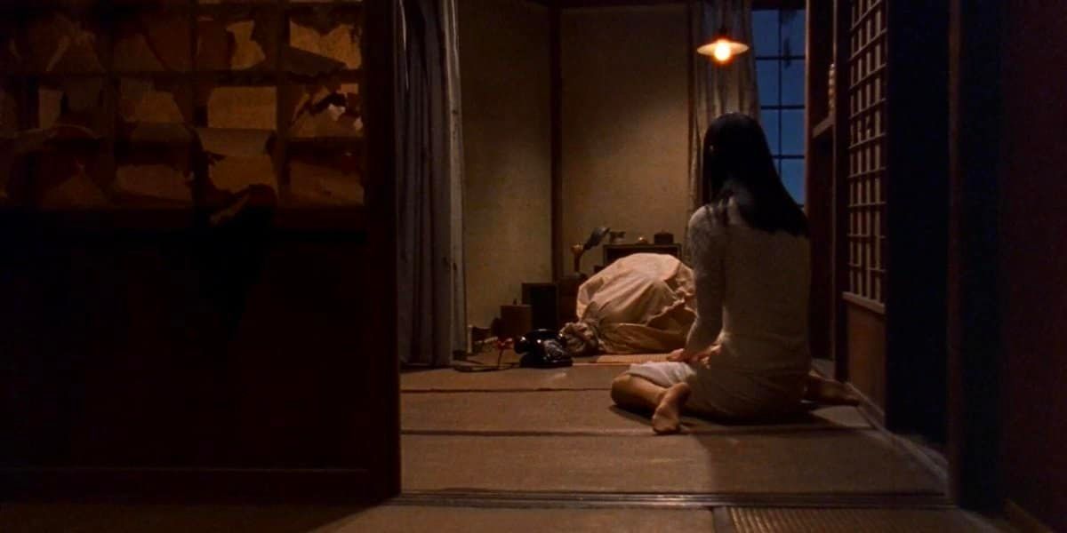 A young woman sits in the floor looking over a bag in the corner of the room.