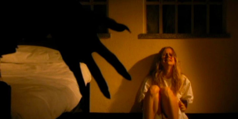 A young woman sits crying against a wall as the shadow of an ominous, clawed hand confronts her. 