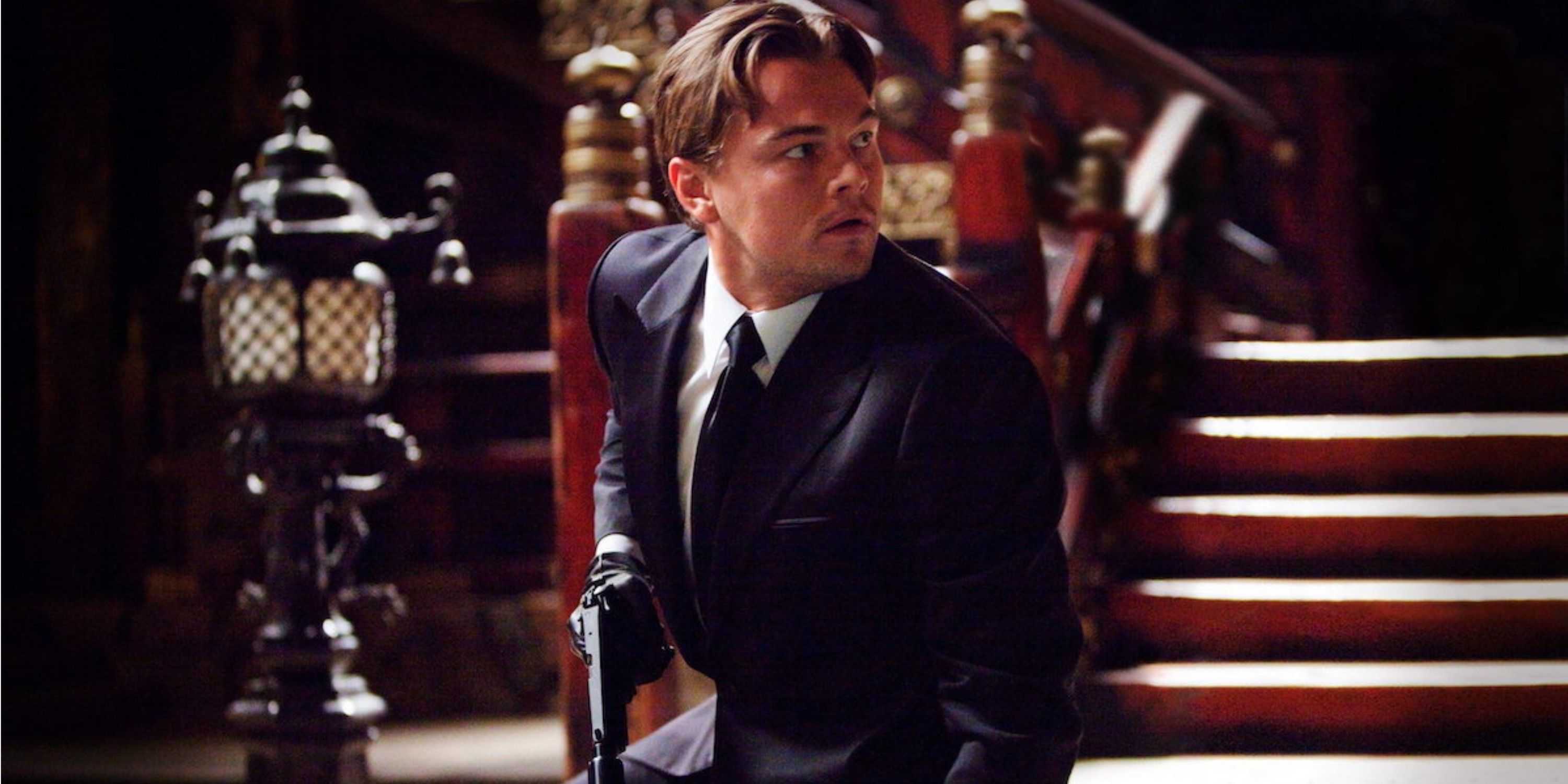 Cobb holding a gun and looking at something off-camera in Inception