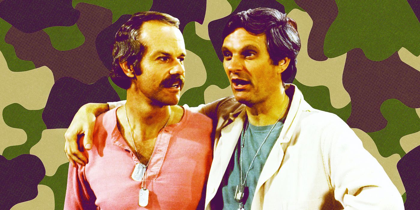 Alan Alda and Mike Farrell embrace against a military camouflage backdrop