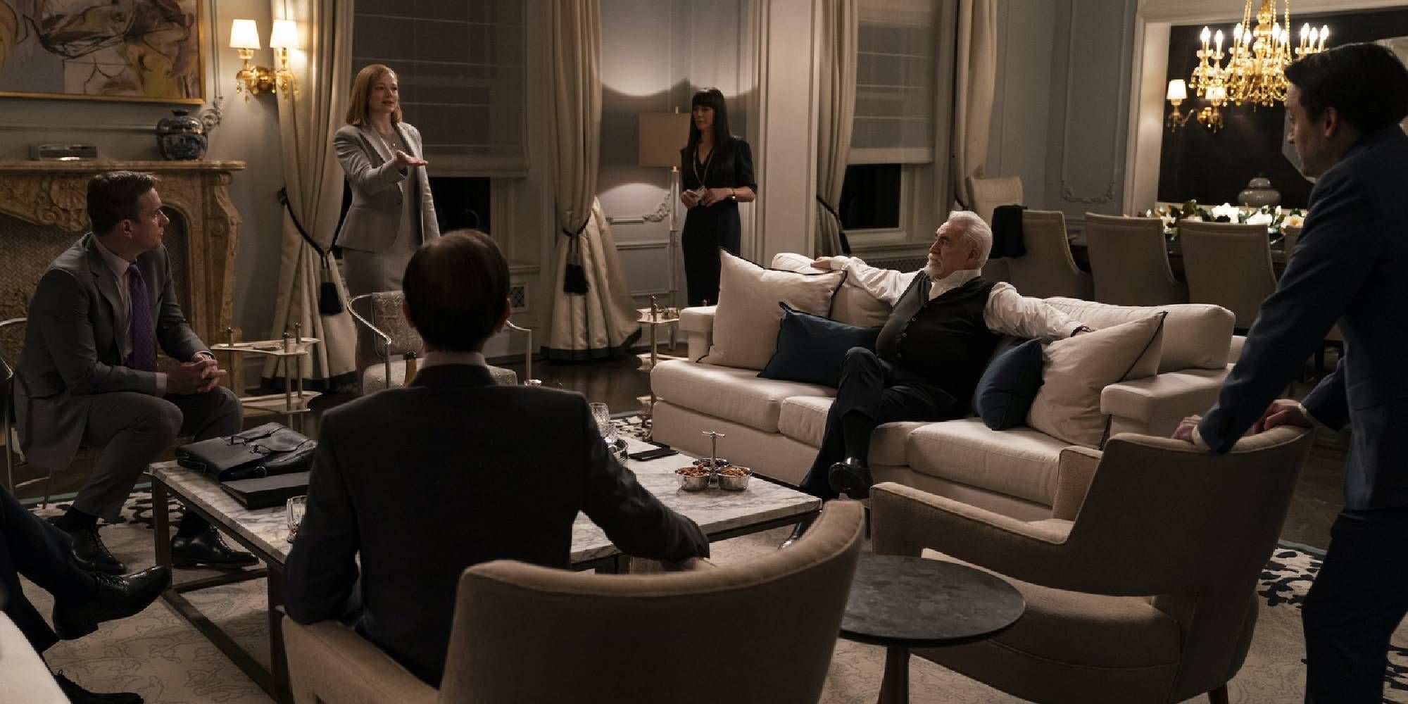 Matthew Macfadyen as Tom Wambsgans, Sarah Snook as Shiv Roy, Zoe Winters as Kerry Castellabate, Brian Cox as Logan Roy, Kieran Culkin as Roman Roy, and Nicholas Braun as Greg all gathered and having a conversation in Succession.